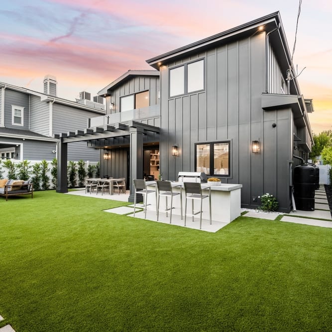 The rear elevation of a modern two-storey home at dusk, seen across its lawn and patio