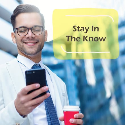 Alliance Lending Services post reading "Stay In The Know" over a man in a light suit smiling at his phone with a coffee cup in his other hand